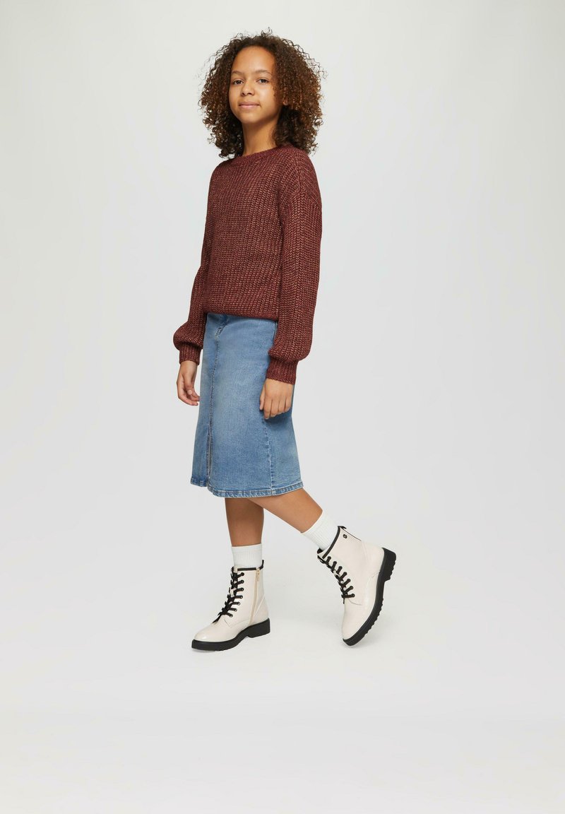 Bordeauxfarbener Strickpullover, hellblaue Jeansrock in knielanger Länge und weiße Kampfstiefel mit schwarzen Schnürsenkeln und Sohlen. Weiße Socken sind oberhalb der Stiefel sichtbar.