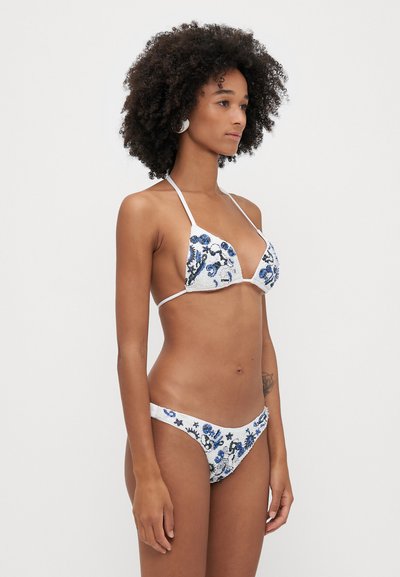 White bikini with blue floral embroidery, featuring a triangular top and minimal coverage bottom. The fabric has a textured appearance.