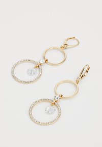 Boucles d'oreilles dorées en métal, présentant des cercles entrelacés, l'un orné de cristaux transparents et d'une gemme pendante. Fini en métal lisse, design élégant.