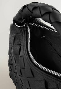 Svart vävd läderväska med ett flätat handtag, silverdragkedja och innerfack. Strukturerad yta med ett geometriskt mönster.