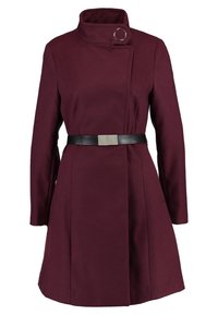 Bordový vlněný kabát s vysokým límcem, zapínáním na jeden knoflík a černým koženým páskem s obdélníkovou kovovou sponou.