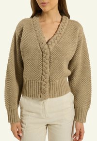 Beige gestrickte Strickjacke mit V-Ausschnitt, strukturiertem Muster und geflochtener Frontschließe. Verkürzte Passform und Rippbündchen am Saum und an den Ärmelabschlüssen.