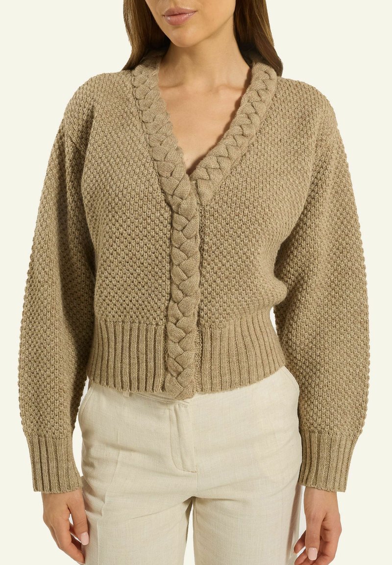 Beige gestrickte Strickjacke mit V-Ausschnitt, strukturiertem Muster und geflochtener Frontschließe. Verkürzte Passform und Rippbündchen am Saum und an den Ärmelabschlüssen.