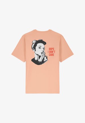 Perzikkleurig T-shirt met een ontspannen pasvorm, voorzien van een zwart grafisch ontwerp van een vrouw en de tekst "OOPS I DON'T CARE" in felrood.