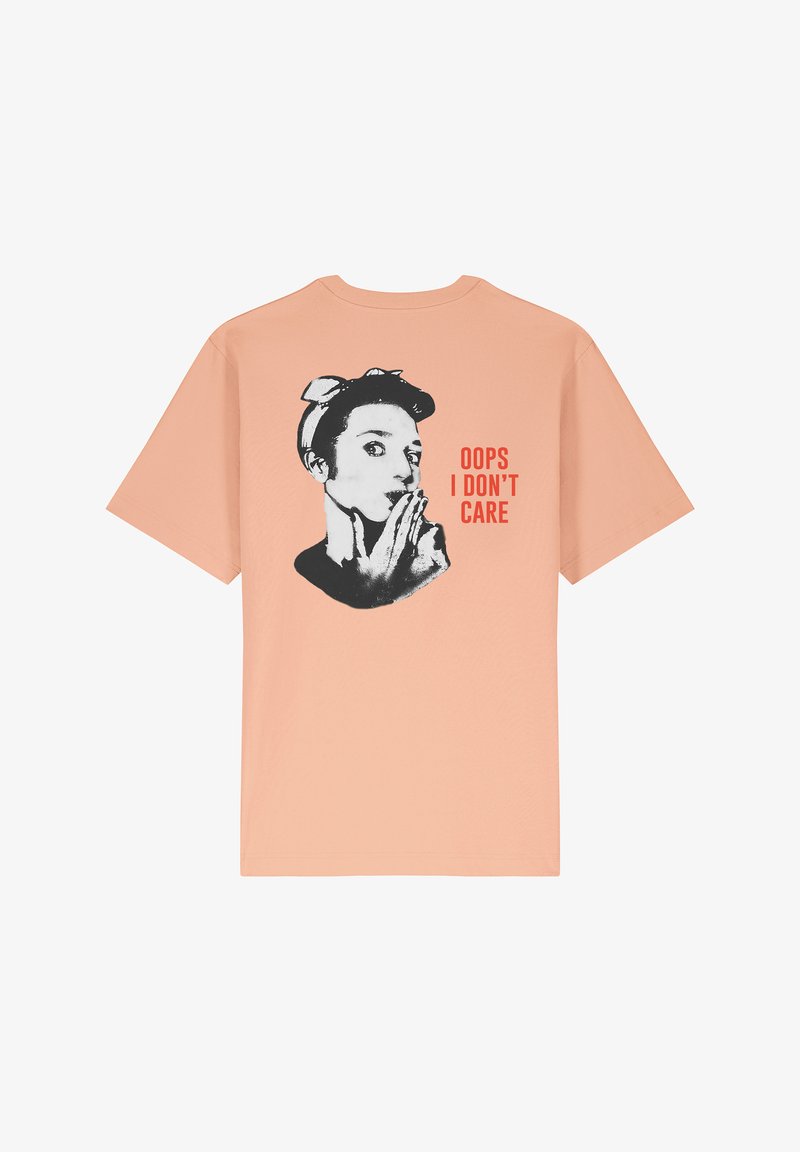 T-shirt pêche avec une coupe décontractée, présentant un graphique noir d'une femme et le texte "OUPS, JE M'EN FOUS" en rouge vif.