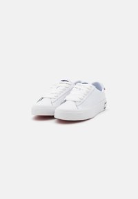 Zapatillas de lona blancas con puntera redonda, suela de goma texturizada y cordones planos. Presenta una marca en la lengüeta y el talón.