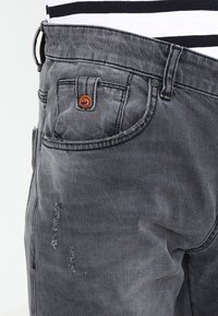 Šedé džíny z denimu s vybledlým vzhledem, s jedním knoflíkem pro zapínání, prošívanými předními kapsami a jemnými opotřebovanými detaily.