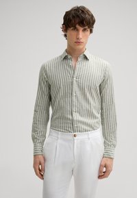 Hellgrünes gestreiftes Hemd aus einem strukturierten Stoff, mit einem Button-Down-Kragen und Manschetten, kombiniert mit weißen, plissierten Hosen.