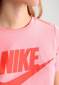 Kortärmad rosa bomulls-t-shirt med en framträdande röd Nike-logotyp och swoosh-design på framsidan. Klassisk rund halsringning.