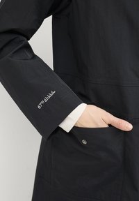 Veste légère marine avec une texture lisse, dotée d'un logo brodé blanc sur la manche et d'un détail à pression sur la poche.