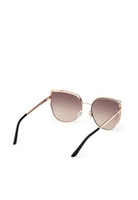 Gafas de sol en forma de ojo de gato con lentes marrones degradados. Montura de metal dorado con varillas negras. Almohadillas nasales transparentes para mayor comodidad. Textura suave y diseño minimalista.