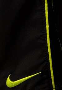 Černé šortky s hladkým povrchem, zdobené neonově žlutým logem Nike a postranním lemováním v neonově žluté barvě.