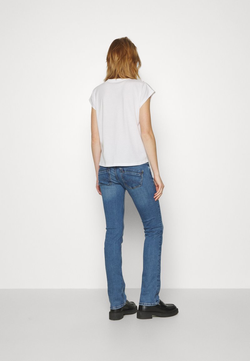 Weißes Kurzarmoberteil und blaue Skinny Jeans. Die Jeans verfügen über ein klassisches Fünf-Taschen-Design, mit einer leichten Waschung und dunklen Stickdetails.