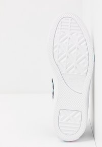 Weißer Gummisohlen mit strukturiertem Profil. Mit geprägtem "Converse All Star"-Logo. Die Seite hat Farbakzente in Türkis.