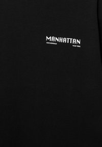 Schwarzer Stoff mit weißem Text "MANHATTAN" zentriert über kleineren Texten "SOHO BOROUGH" und "NEW YORK" im oberen Brustbereich.