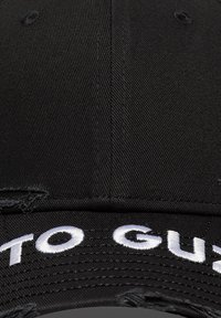 Μαύρο καπέλο με καμπύλη γείσο, με λευκά κεντημένα γράμματα στο μπροστινό μέρος. Το υλικό είναι υφασμάτινο με υφή, με ορατή ραφή και φθαρμένες λεπτομέρειες.