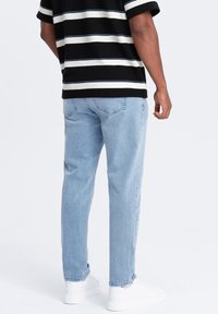 Jeans de mezclilla azul claro con un corte recto, ligeramente desgastados. Combinados con una camisa de rayas en blanco y negro y zapatillas blancas.