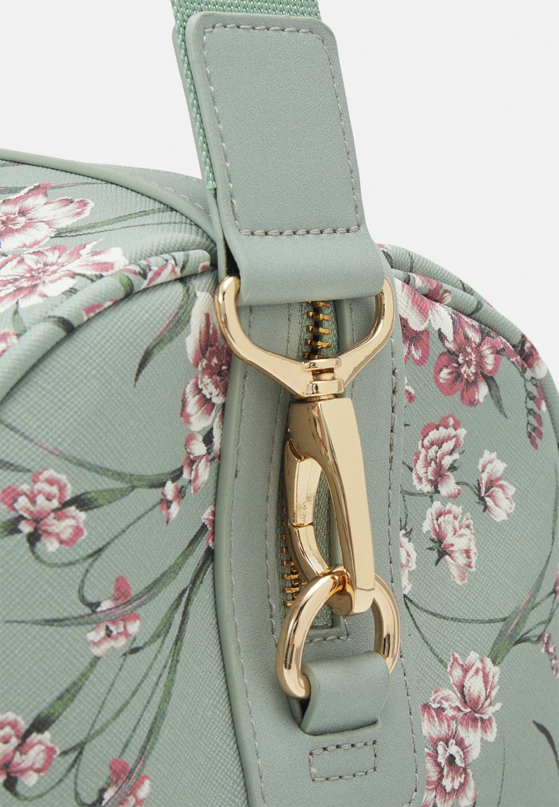 Sac à main vert à motifs floraux avec une finition texturée, doté de quincaillerie dorée, d'une fermeture à clip et d'une bandoulière en tissu durable.