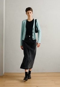 Light blue cardigan over a black top, high-waisted black denim skirt, black socks, and shoes, with hair styled short and accessories visible.