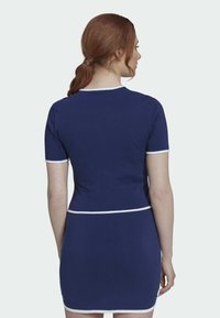 Mörkblå klänning med korta ärmar, med vit kant längs halsringningen och fållen. Figursydd design med en mjuk textur.