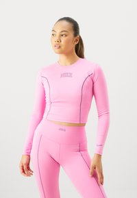 Różowy długi rękaw crop top i dopasowane legginsy wykonane z elastycznego materiału. Posiada logo Nike oraz kontrastujące przeszycia.