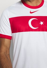 Nike sports jersey in white with a red horizontal band featuring a white crescent moon and star, red sleeves, and a red collar.