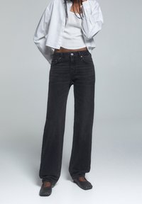 Svarta breda jeans med hög midja, tillverkade av denim, med framfickor och knäppning. I kombination med en vit kortärmad tröja.