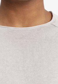 Jasnoszary sweter z dzianiny z okrągłym dekoltem, subtelną fakturą i gładkim wykończeniem. Widać detale szwów na ramionach.