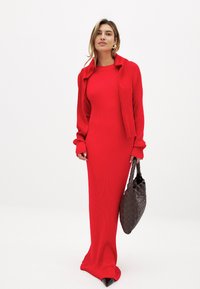 Sarkans ribots džersijs garais kleita ar pieguļošu siluetu, akcentēta ar atbilstošu šalli. Melni norādītā pirksta apavi un austs brūns rokassoma noslēdz izskatu.