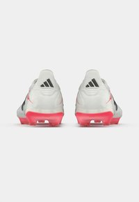 Ποδόσφαιρικα παπούτσια με λευκή επένδυση, μαύρες λεπτομέρειες και ροζ ημιδιαφανείς σόλες με αιχμηρές καρφίτσες για πρόσφυση.