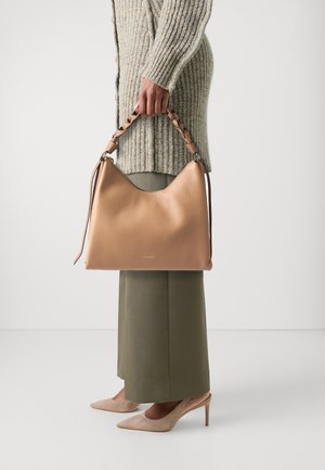 Borsa in pelle color nocciola con forma curvata e manici intrecciati. La borsa presenta una superficie testurizzata e dettagli lisci, abbinata a un maglione in maglia e pantaloni.