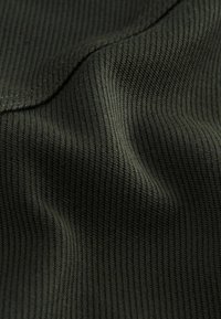 Ribbed kangas sügavas oliivrohelises värvitoonis, millel on pehme tekstuur ja väljaulatuvad jooned, tuues esile valguse ja varju variatsioonid pinnal.