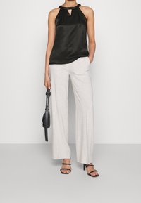 Černý saténový top na zavazování za krk s detailem klíčové díry, v kombinaci se světle šedými lněnými širokými kalhotami. Černé sandály na podpatku a malá černá kabelka.