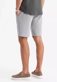 Shorts gris clair en tissu texturé, avec poches latérales et coupe droite. Portés avec des chaussures brunes à enfiler et un shirt gris foncé.