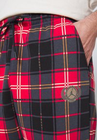 Röda och svarta rutiga shorts med dragsko i midjan, ficka och en cirkulär logotyp med en basketbollssilhuett. Mjuk tygstruktur.