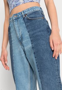 Jeans i denim med en färgblockdesign som har en ljusblå vänster sida och en mörkblå högersida. Standard midja med synlig sömnad.