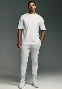 Biely bavlnený tričko s krátkymi ruk�ávmi v kombinácii so svetlo šedými joggermi z mäkkej tkaniny. Biely tenisky dotvárajú celý outfit.