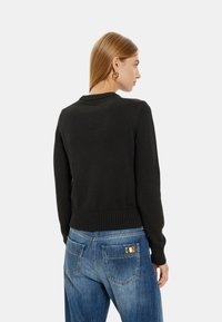 Maglione nero a maglia con orlo e polsini a coste, mostrato da dietro, abbinato a jeans blu a vita alta con due tasche posteriori.