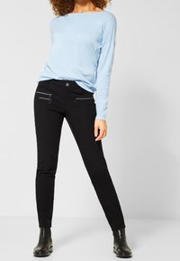 Svarta åtsittande byxor med dragkedjefickor och knäppning, i kombination med en ljusblå långärmad topp. Strukturerad textil och smal silhuett.