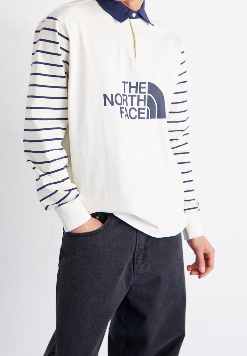 Pánský polo svetr s dlouhým rukávem v krémové barvě, s námořnickými vodorovnými pruhy na rukávech, námořnickým límečkem a výrazným námořnickým logem na hrudi.