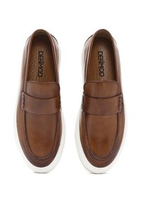 Zapatos marrones de cuero tipo mocasín con una suela plana de goma blanca, que presentan una puntera cosida y una correa decorativa a lo largo del empeine.