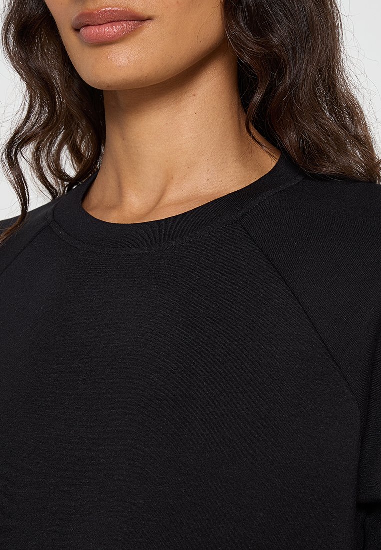 Zwart sweatshirt met een ronde hals, raglanmouwen en een zachte, gestructureerde stof. Soepele stikseldetails langs de halslijn.