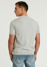 Lichtgrijze gebreide sweater met korte mouwen en subtiele textuur, met een ronde hals en zijsplitten, gedragen met blauwe denim jeans.