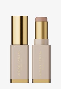 Foundation stick with a gold cap and base, featuring a beige tube with gold lettering. Smooth texture, minimalist design.