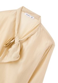 Blusa di raso crema con un fiocco annodato al colletto, maniche lunghe, texture liscia e un sottile lucido. Etichetta con il marchio "Terranova," taglia S.