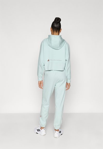 Φωτεινή μέντα πράσινη cropped φούτερ με λογότυπο στην πλάτη και ταιριαστά παντελόνια jogger. Μαλακό ύφασμα, ελαστικά μανσέτες και κεντημένες λεπτομέρειες στα πόδια. Λευκά αθλητικά παπούτσια.