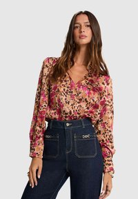 Blouse à manches longues en satin, avec un motif floral rose et marron sur fond beige. Encolure en V et coupe ample.