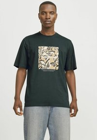 Camiseta de algodón negra con manga corta, que presenta un estampado gráfico beige con motivos botánicos y texto en un marco rectangular en la parte delantera.