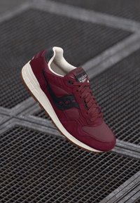 Burgunderfargede sneakers med svarte detaljer, mesh- og semsket skinnmaterialer, polstret såle og snøredesign. Har logo på tungen og mønstret tekstur.