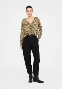 Blusa de estampado de leopardo en tonos neutros, con botones, combinada con pantalones negros de cintura alta y botas negras hasta el tobillo con tachas.